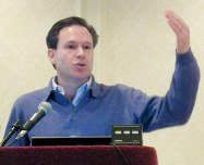 Man without tie speaking with hand raised to make a point