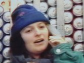 Woman with knit hat standing in front of cans of soda trying to talk on phone
