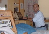 Don behind bed and hospital equipment at his laptop looking at the camera