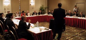 Many people around a U-shaped table listening to someone present