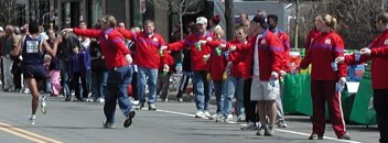 Line of people in red jackets holding cups of water with one runner shown taking it on the run