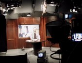 Studio with Dan at desk in front of background, lights, camera, monitor