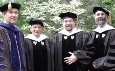 Four guys in robes and funny hats smiling at the camera