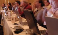 Row of laptops and people using them and listening to speakers