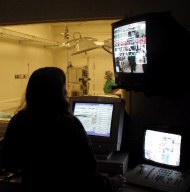 View from inside dark room showing TV and computer monitors and window into simulation