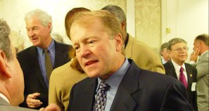 John with suit, blue tie and shirt, talking to someone with others talking to each other