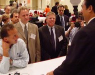 People in suits looking up at Ted on the podium