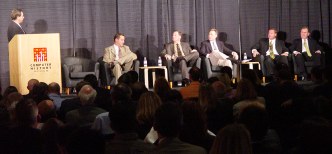 Robert standing behind lectern, five people sitting, backs of heads of people in the audience