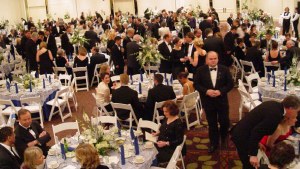 Lots of tables with people in black tie and gowns standing around